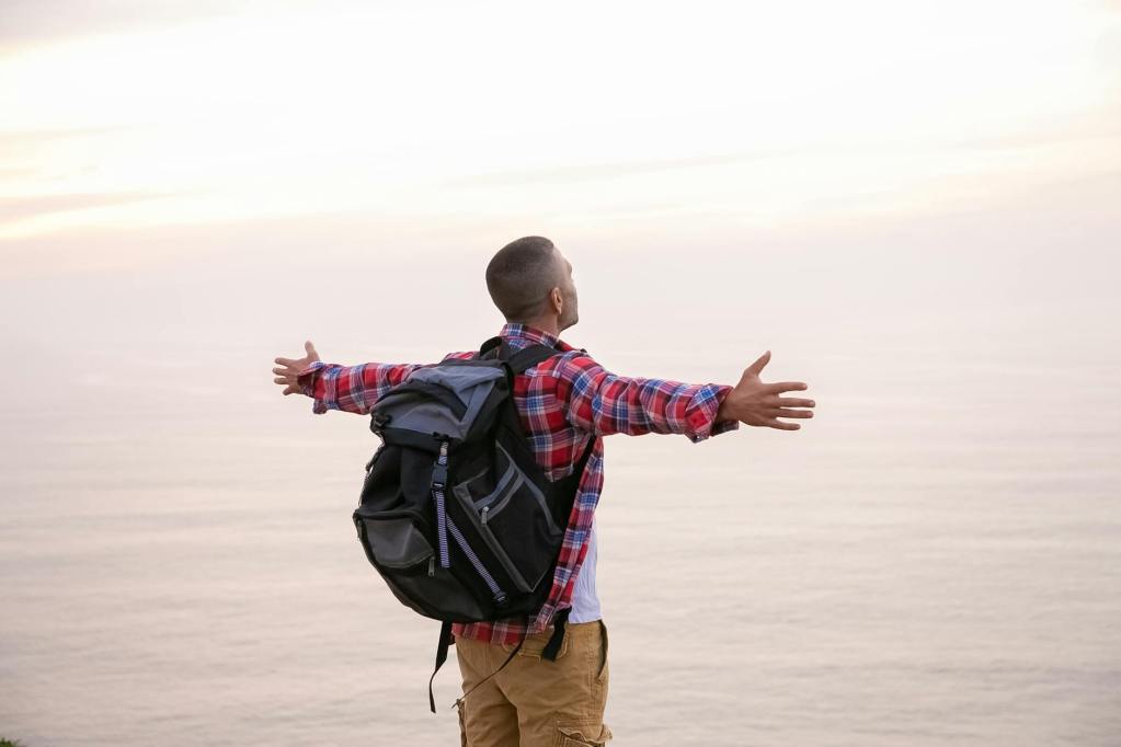 man in red plaid long sleeves carrying backpack stretching his arms