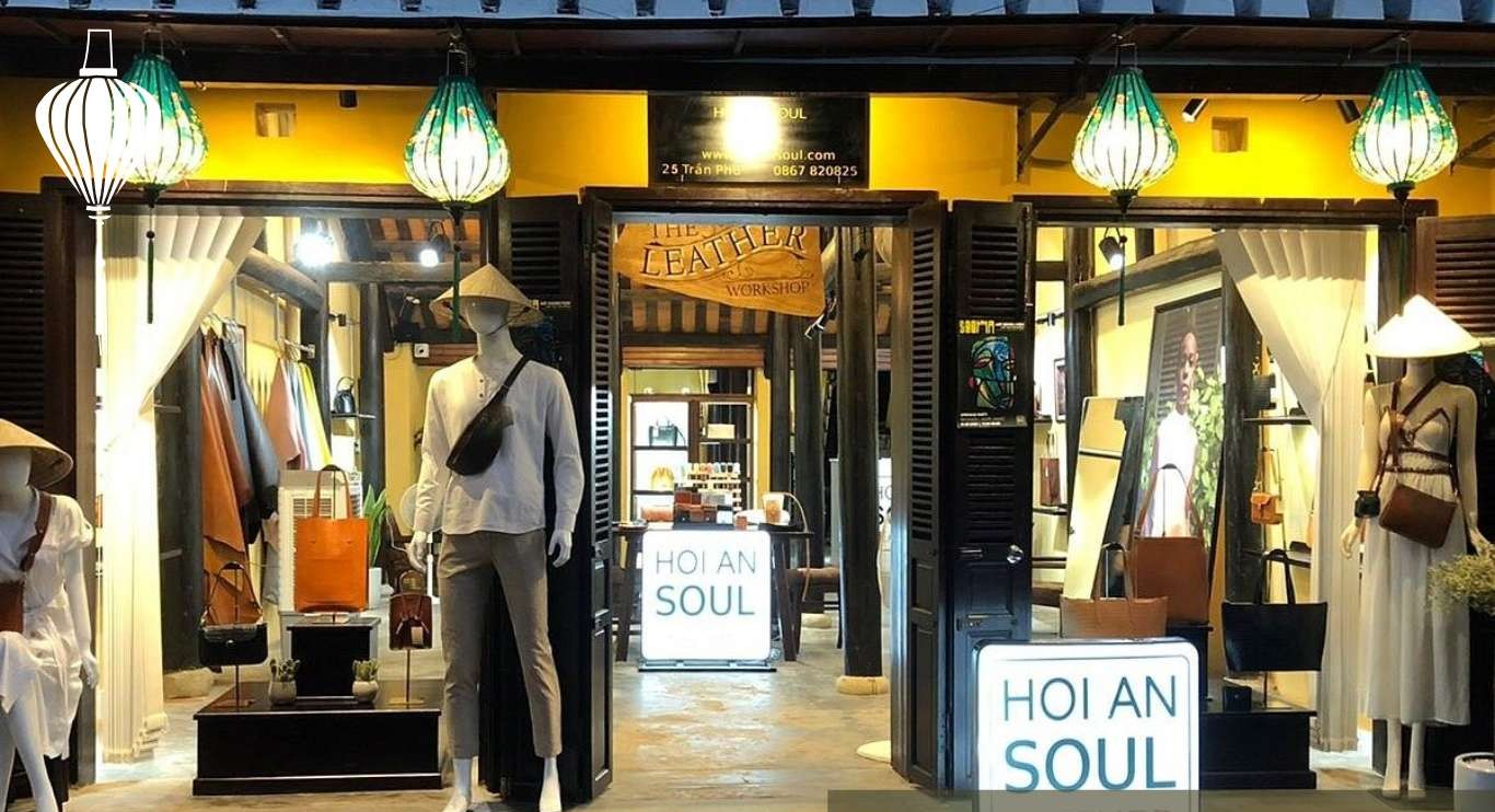 A view of a storefront titled 'HOI AN SOUL' featuring mannequins dressed in fashionable clothing, leather goods displayed, and traditional lanterns hanging above.